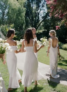 four bridesmaids in white dresses walking down the sidewalk