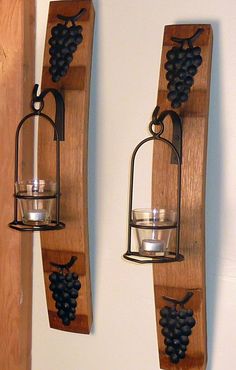 two wine glasses are hanging on the wall next to a candle holder that has grapes attached to it