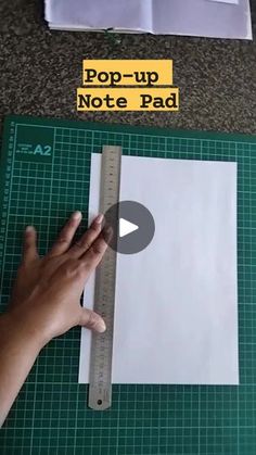 someone is cutting paper with a ruler on top of it and another piece of paper next to them