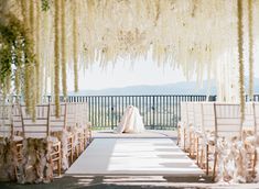 an outdoor ceremony setup with white chairs and wistery trees hanging from the ceiling