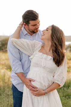 a man and woman standing next to each other while holding their hands on their pregnant belly