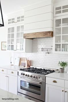 a kitchen with white cabinets and stainless steel stove top oven, range hood, and overhead lighting