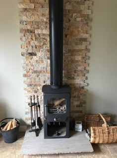 a wood burning stove sitting in front of a brick wall next to a basket of firewood