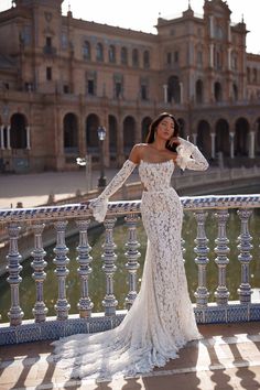 a woman in a white dress standing on a balcony next to a fountain and looking off into the distance