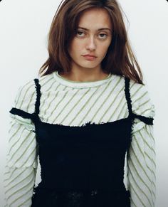 a woman with brown hair wearing a white and black sweater is looking at the camera