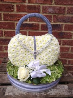 a white purse sitting on top of a wooden table next to a brick wall with flowers in it