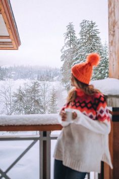 a woman standing on top of a balcony next to a snow covered forest