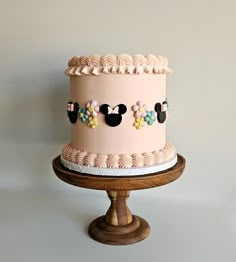 a pink cake with mickey ears on it sitting on top of a wooden stand in front of a white wall