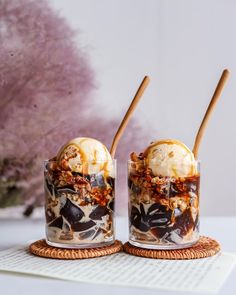 two glasses filled with ice cream and toppings on top of a table next to a book