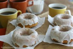 four glazed donuts sitting on top of napkins next to two cups of coffee