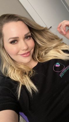 a woman with long blonde hair is brushing her hair and looking at the camera while smiling