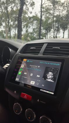 the dashboard of a car with an electronic device in it's center console and trees in the background