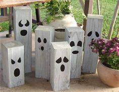 several cement blocks with faces painted on them sitting next to flowers and potted plants