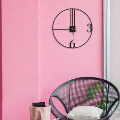 a pink wall with a black clock on it and a wicker chair in the foreground