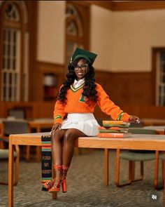 a woman sitting on top of a wooden table with books in front of her and wearing an orange sweater