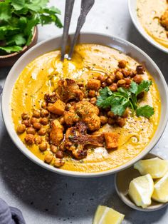 two bowls filled with yellow soup and garnished with cilantro, parsley and lemon wedges