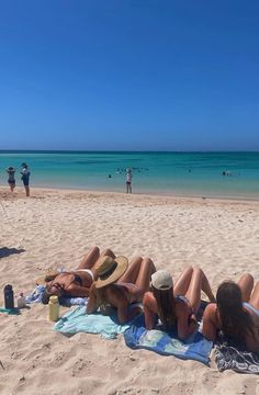 two women laying on the beach with their backs to each other, while one woman stands in the background