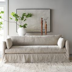 a white couch sitting next to a window in a living room under a painting on the wall