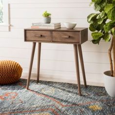 a wooden table with two drawers and a potted plant next to it on a rug