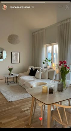 a living room filled with furniture and flowers on top of a wooden table in front of a window