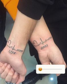 two people are holding hands with tattoos on their wrists and one has a heart in the middle