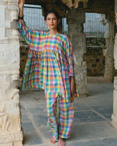 a woman standing in front of a stone structure wearing colorful clothing and sandals on her feet