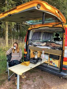 a woman sitting at a picnic table in the back of a yellow van with its doors open