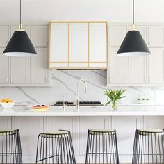 three black and white pendant lights hanging over a kitchen island with four stools in front of it