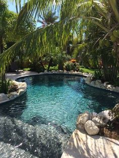 an outdoor swimming pool surrounded by palm trees and rocks with water running down the side