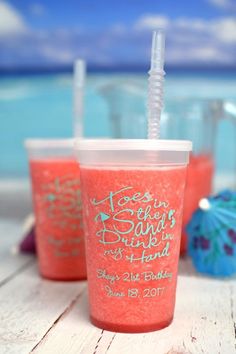 three plastic cups with straws sitting on a table next to an umbrella and the ocean