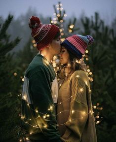 a man and woman standing next to each other in front of a christmas tree with lights