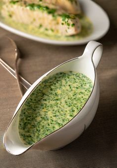 two white plates with food on them and spoons next to one plate that has broccoli soup in it