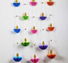 an assortment of colorful paper fans hanging from hooks on a white wall with gold accents