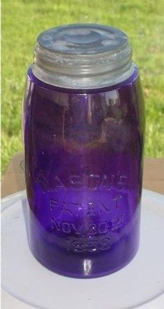 a purple mason jar sitting on top of a white table next to a green field