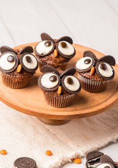 chocolate cupcakes decorated with googly eyes on a wooden platter next to oreos