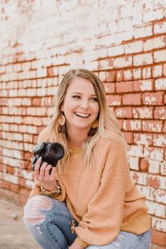 a woman sitting on the ground with a camera in her hand and smiling at the camera