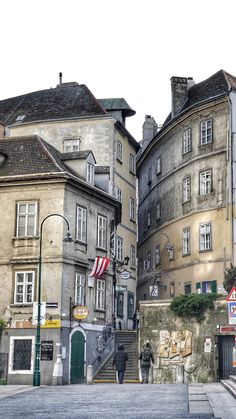 two people are walking down the street in front of some old buildings with flags on them