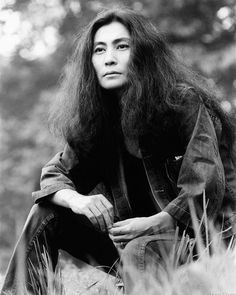 an old photo of a woman with long hair sitting on the ground in front of trees