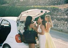 three women standing next to a car with their trunk open and one woman in the back