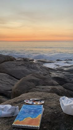 there is a book on the rocks by the ocean with an orange sky in the background