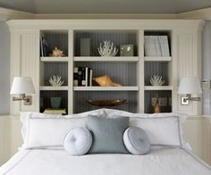 a bed with white sheets and pillows in a room that has shelving on the wall