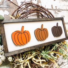 three pumpkins cut out on a wooden sign in front of some flowers and branches