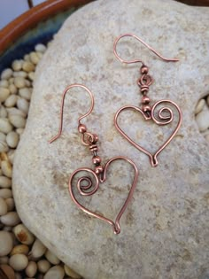 two heart shaped copper earrings sitting on top of a rock next to some rocks and pebbles