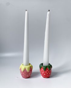 two candles with strawberries on them sitting next to each other