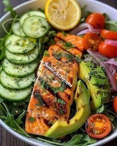 a salad with salmon, avocado, tomatoes and cucumbers in it