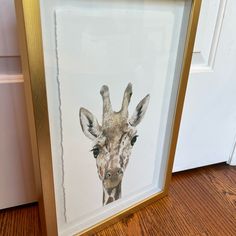 a giraffe's head is framed in a gold frame on the floor