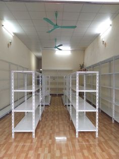 empty shelves in a large room with wooden floors and ceiling fan mounted to the ceiling