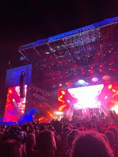 a large group of people standing on top of a stage with bright colored lights at night