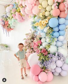 a little boy standing in front of a giant balloon wall with flowers and balloons all over it