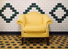 a yellow chair sitting in front of a white brick wall with black and green tiles